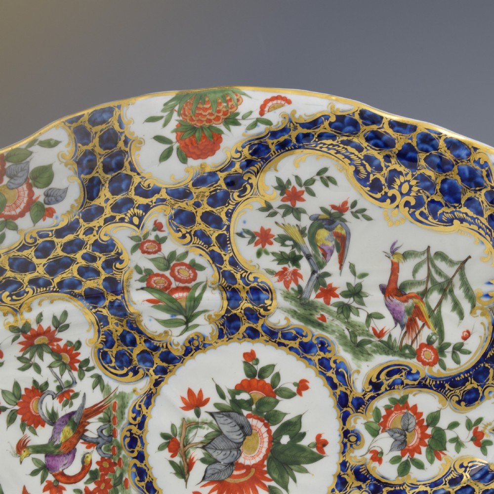 An eighteenth-century Worcester soft-paste porcelain leaf-shaped dish decorated with dark blue cailloute ground, gilded reserves, and hand-painted Kakiemon floral and bird motifs. View IV