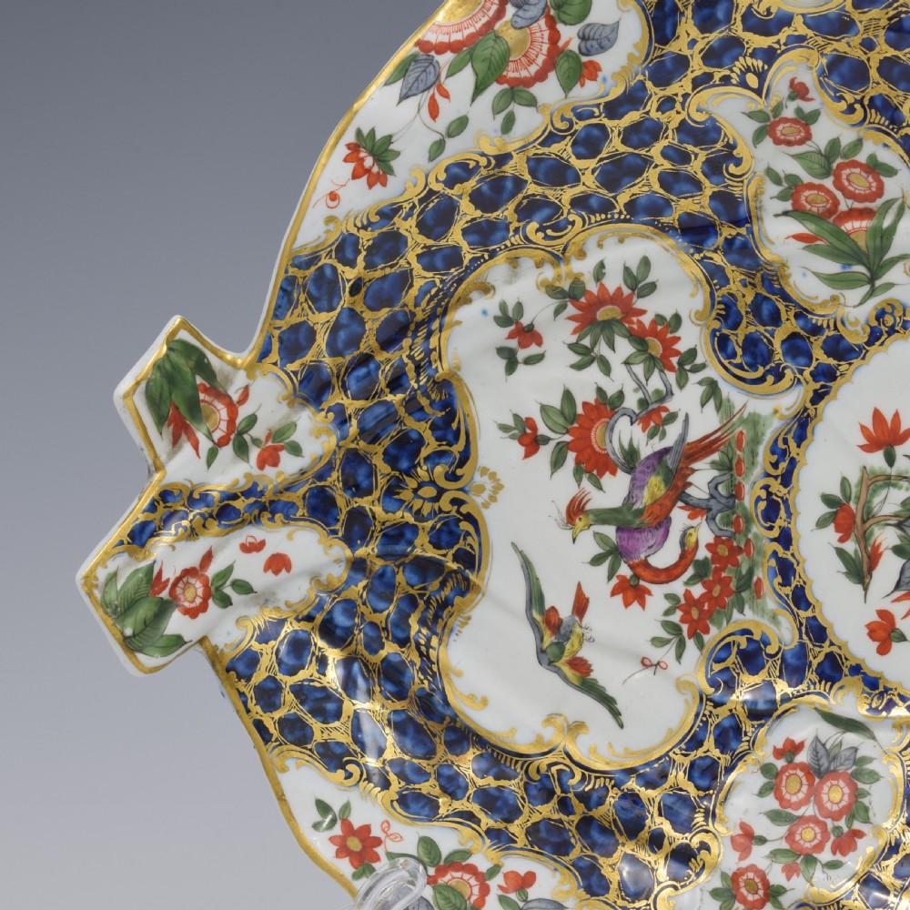 An eighteenth-century Worcester soft-paste porcelain leaf-shaped dish decorated with dark blue cailloute ground, gilded reserves, and hand-painted Kakiemon floral and bird motifs. View V
