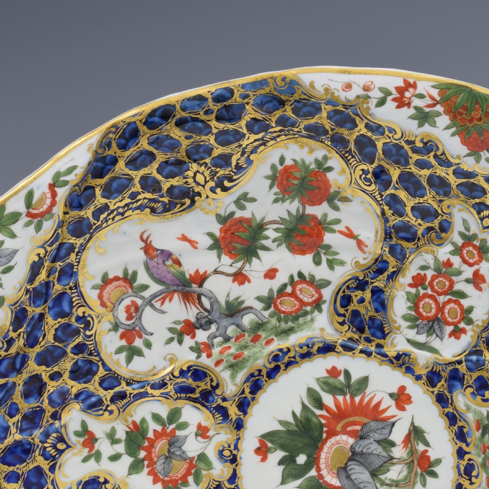 An eighteenth-century Worcester soft-paste porcelain leaf-shaped dish decorated with dark blue cailloute ground, gilded reserves, and hand-painted Kakiemon floral and bird motifs. View VI