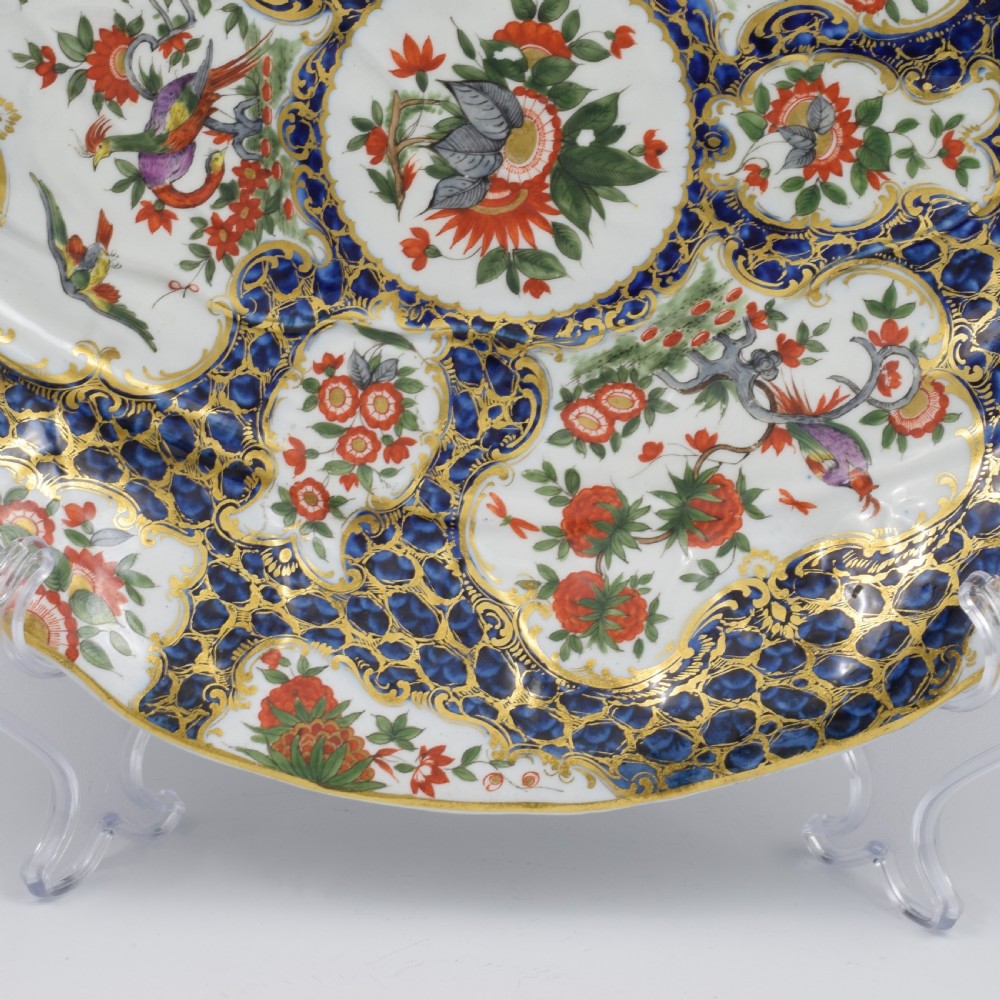 An eighteenth-century Worcester soft-paste porcelain leaf-shaped dish decorated with dark blue cailloute ground, gilded reserves, and hand-painted Kakiemon floral and bird motifs. View VII
