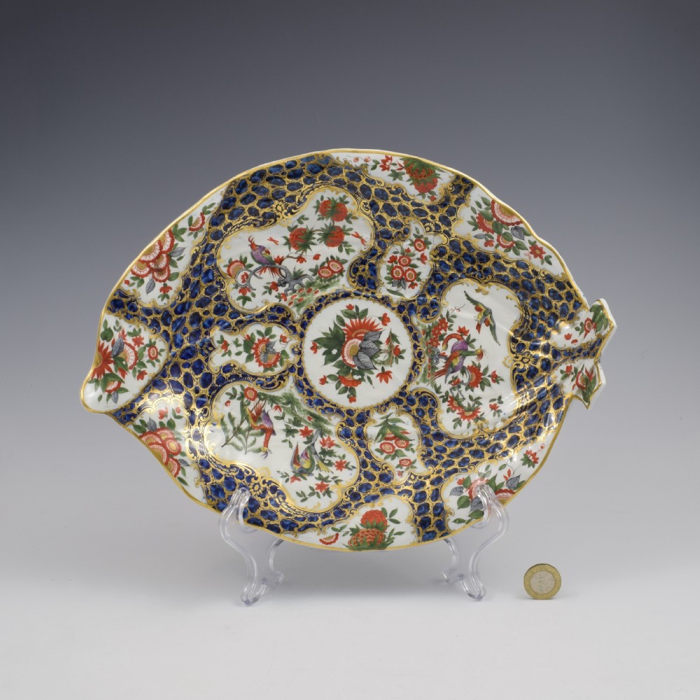 An eighteenth-century Worcester soft-paste porcelain leaf-shaped dish decorated with dark blue cailloute ground, gilded reserves, and hand-painted Kakiemon floral and bird motifs. View IX