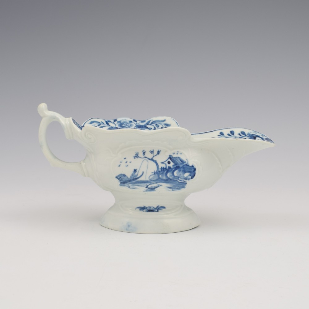 An 18th-century First Period Worcester soft-paste porcelain sauce boat decorated with a hand-painted blue and white chinoiserie landscape motif.