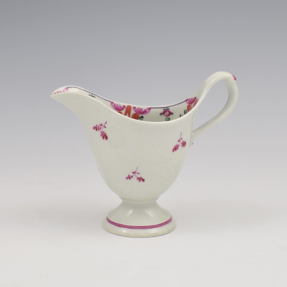 An 18th-century Georgian New Hall white porcelain cream jug featuring a high clip handle, pedestal foot, and hand-painted pink floral motifs. View II