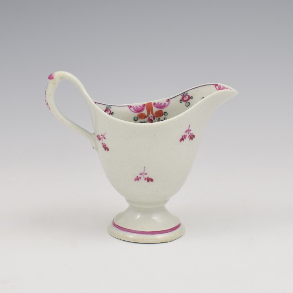 An 18th-century Georgian New Hall white porcelain cream jug featuring a high clip handle, pedestal foot, and hand-painted pink floral motifs. View V