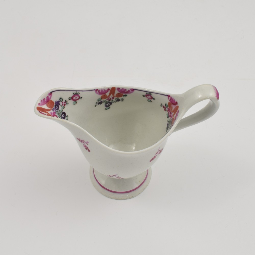 An 18th-century Georgian New Hall white porcelain cream jug featuring a high clip handle, pedestal foot, and hand-painted pink floral motifs. View VI