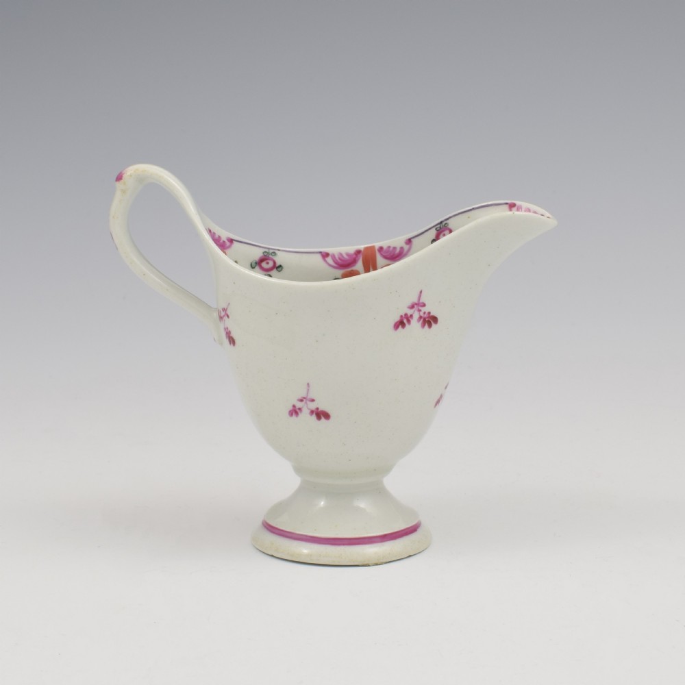 An 18th-century Georgian New Hall white porcelain cream jug featuring a high clip handle, pedestal foot, and hand-painted pink floral motifs. View IX