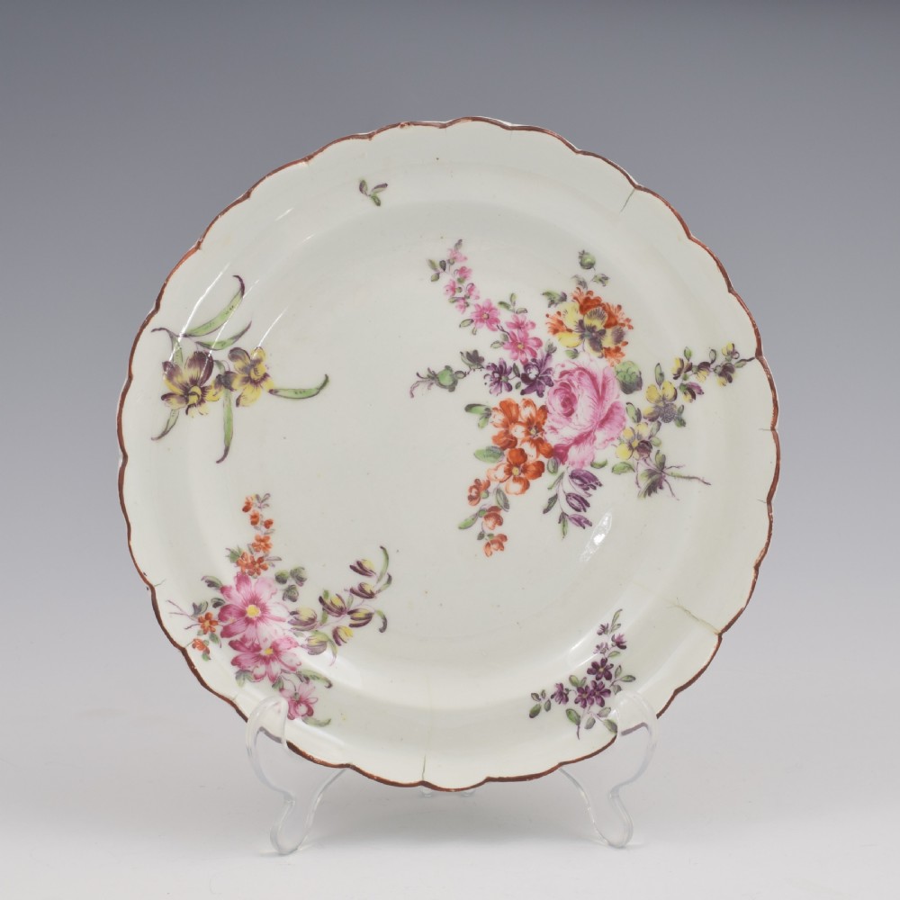 An 18th-century English soft-paste porcelain lobed plate decorated with hand-painted polychrome floral sprays and a brown line rim.