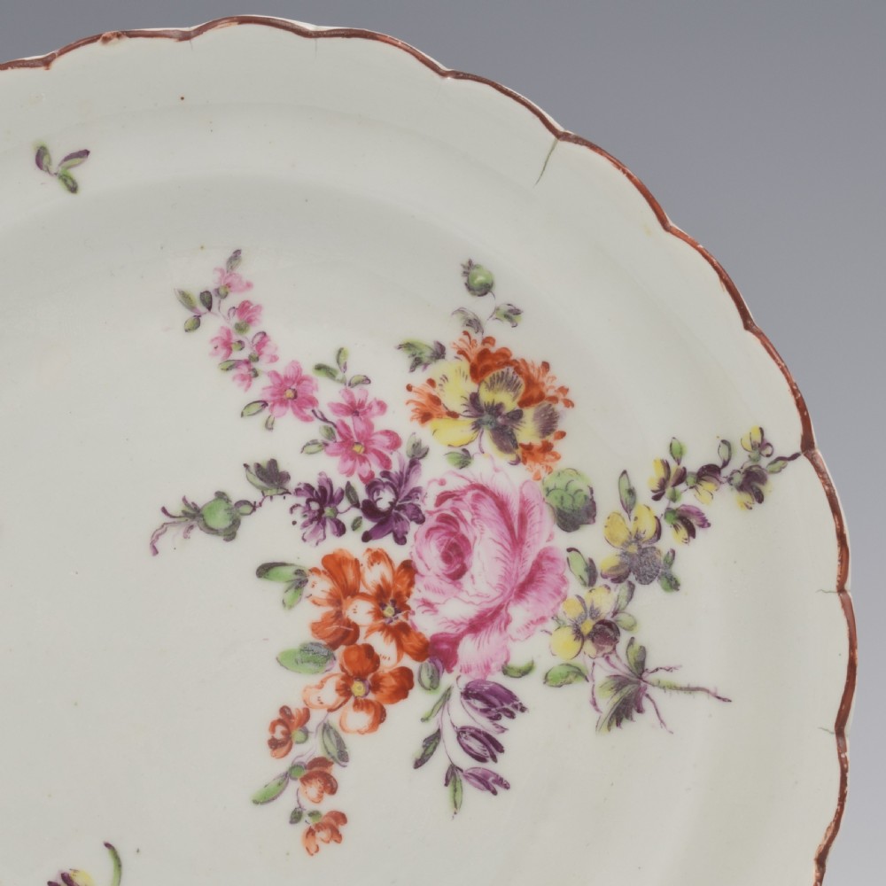 An 18th-century English soft-paste porcelain lobed plate decorated with hand-painted polychrome floral sprays and a brown line rim. View II