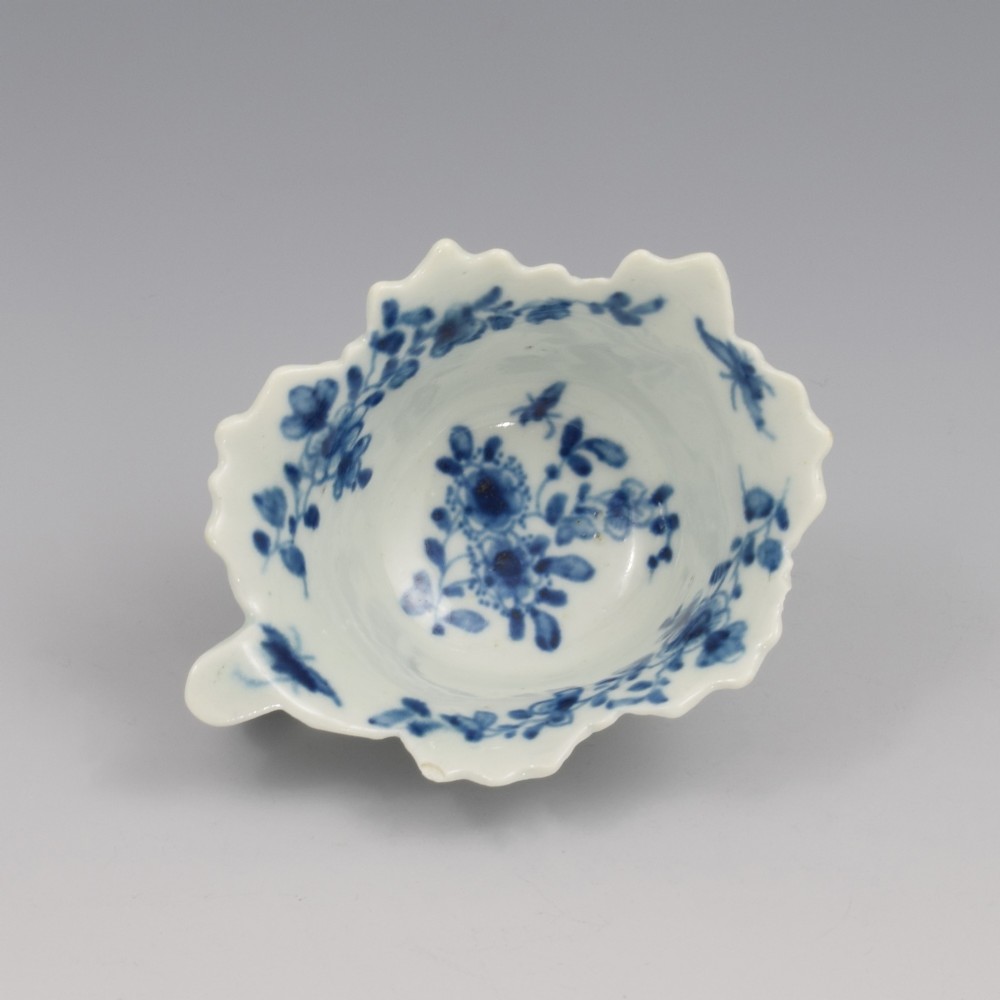 A leaf-shaped soft-paste porcelain butter boat decorated with an underglaze blue floral pattern and serrated edges.
