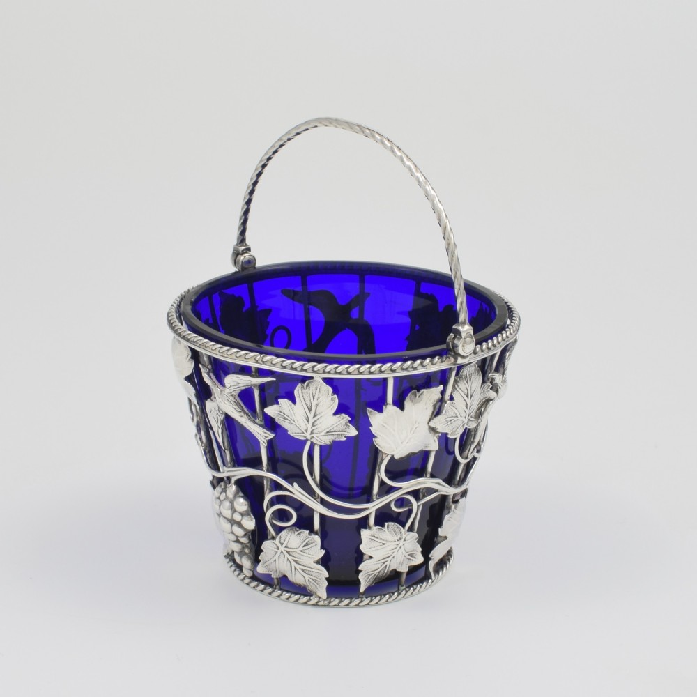 A Georgian sterling silver wirework cream pail featuring botanical motifs and a twisted overhead handle, fitted with a cobalt blue glass liner. View IV