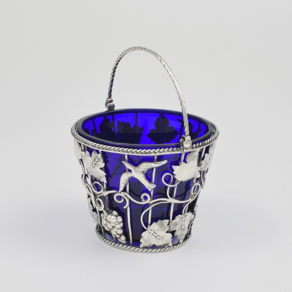 A Georgian sterling silver wirework cream pail featuring botanical motifs and a twisted overhead handle, fitted with a cobalt blue glass liner. View VIII
