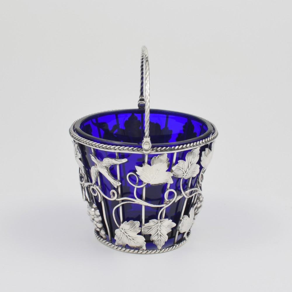 A Georgian sterling silver wirework cream pail featuring botanical motifs and a twisted overhead handle, fitted with a cobalt blue glass liner. View IX