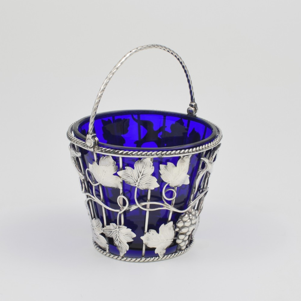 A Georgian sterling silver wirework cream pail featuring botanical motifs and a twisted overhead handle, fitted with a cobalt blue glass liner. View X