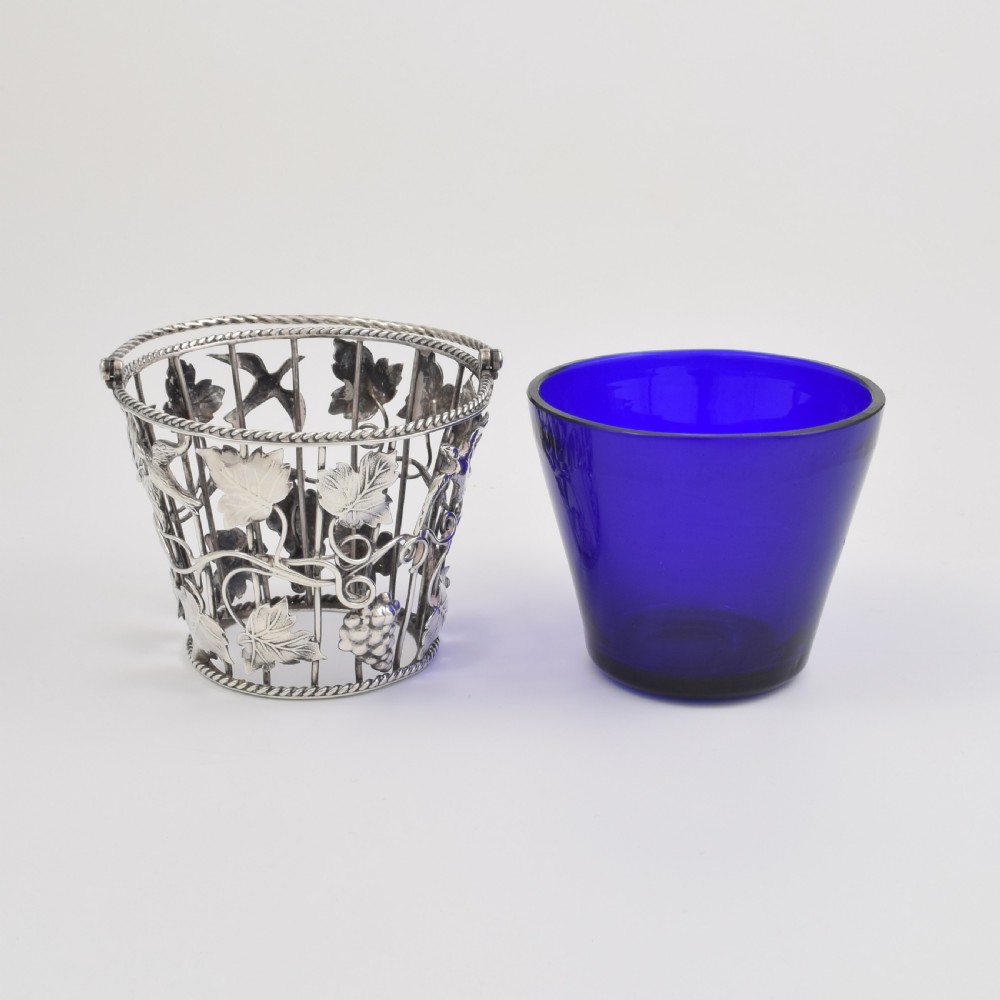 A Georgian sterling silver wirework cream pail featuring botanical motifs and a twisted overhead handle, fitted with a cobalt blue glass liner. View XII