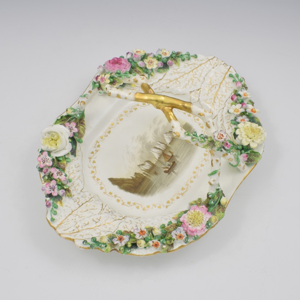 A white porcelain basket decorated with hand-sculpted flowers along the rim, a gilded twig-shaped handle, and a hand-painted marine landscape scene in the centre. View III
