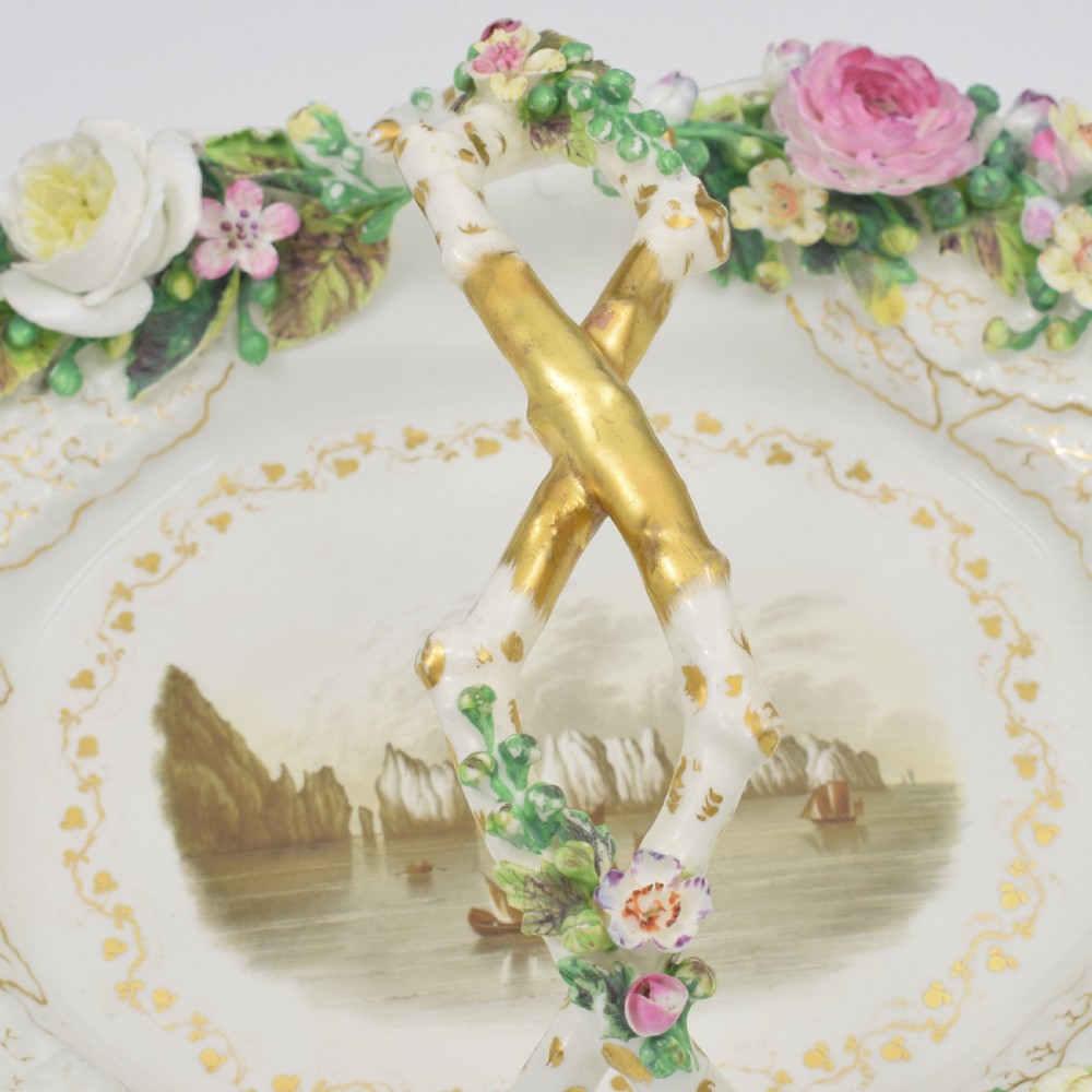 A white porcelain basket decorated with hand-sculpted flowers along the rim, a gilded twig-shaped handle, and a hand-painted marine landscape scene in the centre. View XI