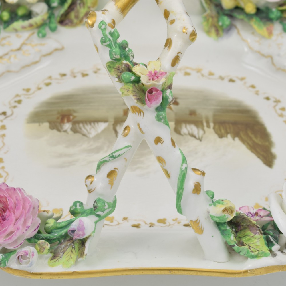 A white porcelain basket decorated with hand-sculpted flowers along the rim, a gilded twig-shaped handle, and a hand-painted marine landscape scene in the centre. View XIII