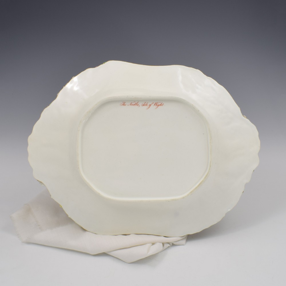 A white porcelain basket decorated with hand-sculpted flowers along the rim, a gilded twig-shaped handle, and a hand-painted marine landscape scene in the centre. View XV