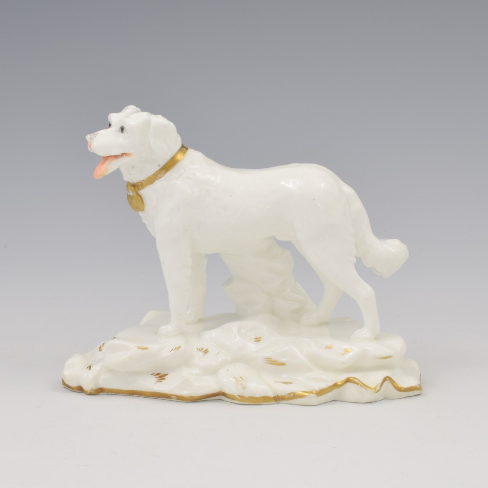 A white glazed porcelain figure of a standing gundog on a molded base with gold gilded accents along the collar and base rim.
