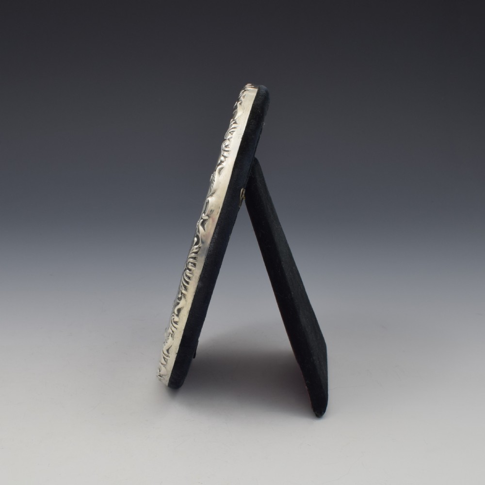 An oval silver photo frame with embossed foliate scrolling decoration surrounding a dark purple aperture. View V