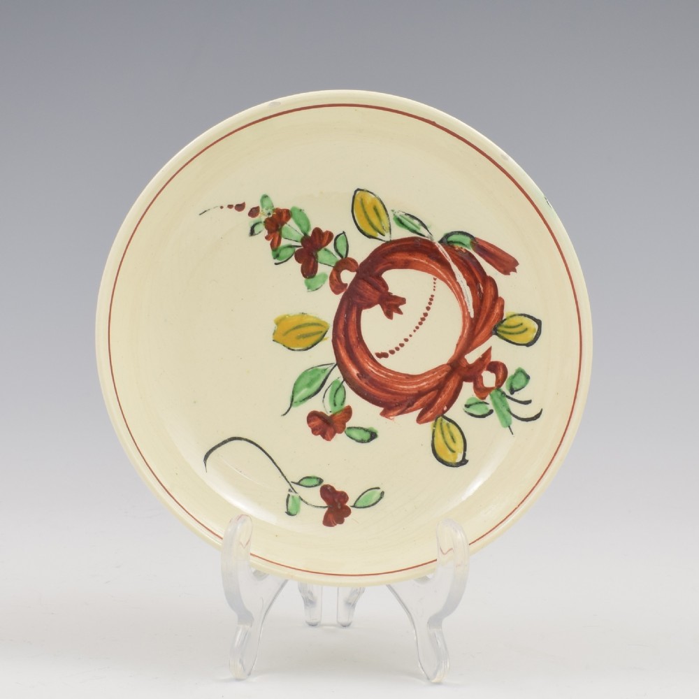 An antique creamware tea cup and saucer featuring hand-painted red, green, and yellow floral motifs in the Kings Rose pattern against a light cream backdrop. View II