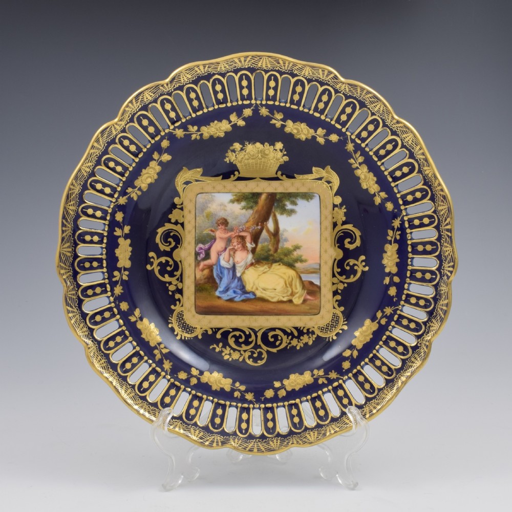 A cobalt blue and gilt porcelain cabinet plate featuring a pierced reticulated border and a central hand-painted square scene of Cupid and Psyche.