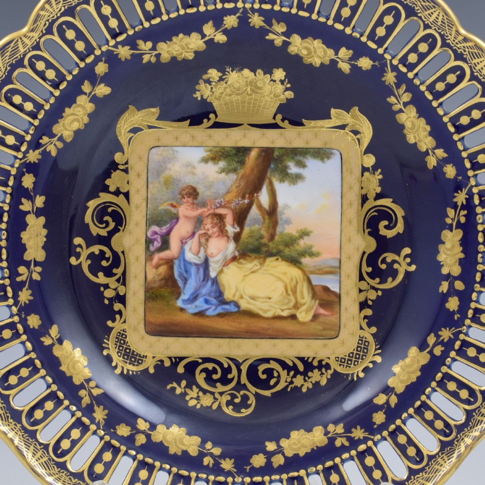 A cobalt blue and gilt porcelain cabinet plate featuring a pierced reticulated border and a central hand-painted square scene of Cupid and Psyche. View II