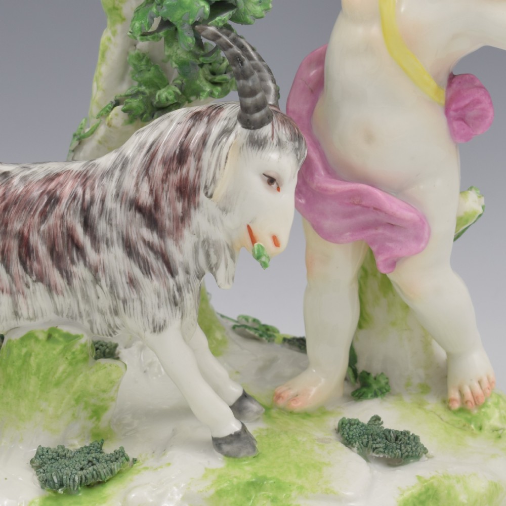 A pair of hand-painted porcelain figures featuring young putti standing alongside goats amidst green leafy foliage on rounded naturalistic bases. View XXII