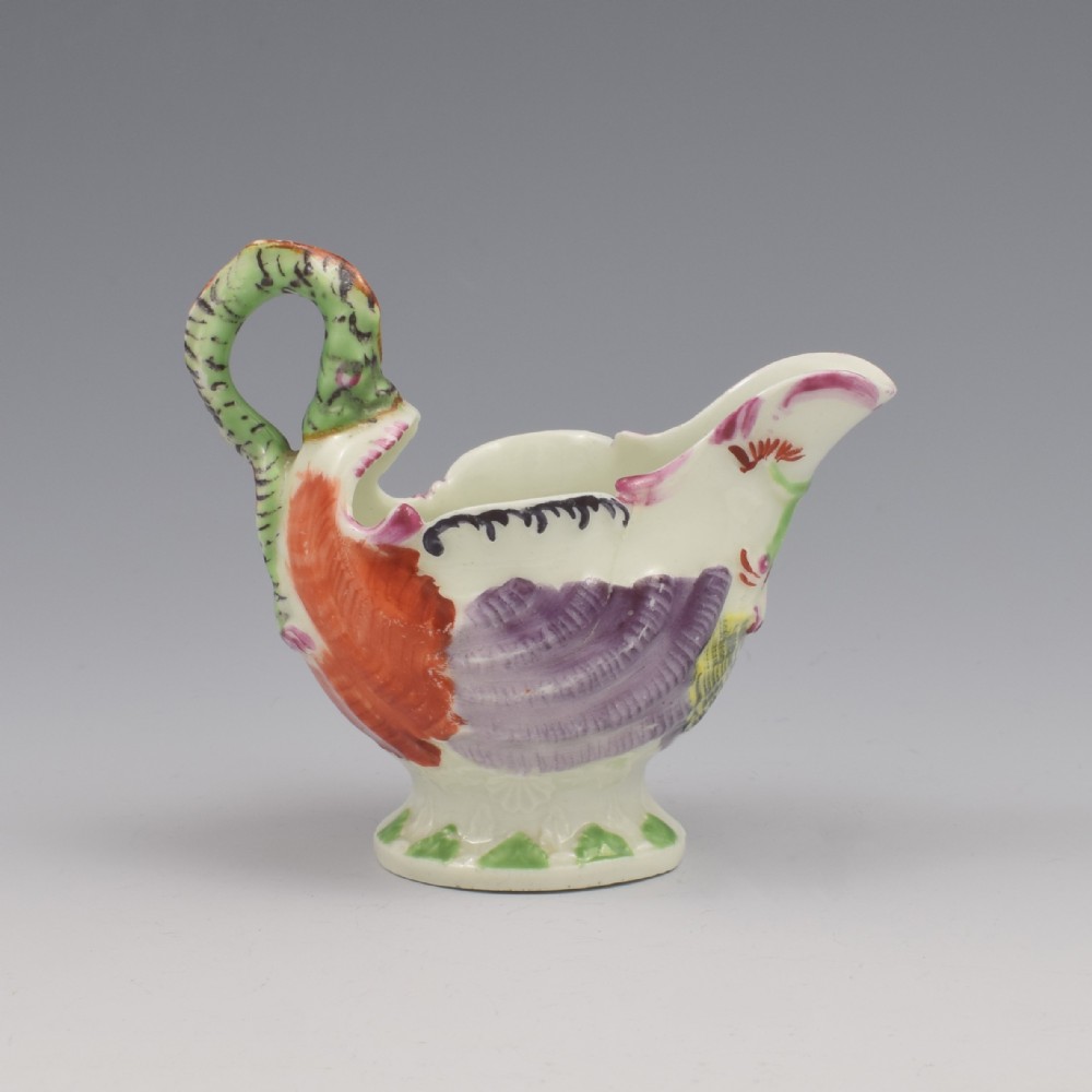 An 18th-century First Period Worcester soft-paste porcelain cream boat featuring a green lamprey eel handle, shell-moulded body painted in polychrome enamels, resting on a pedestal base.