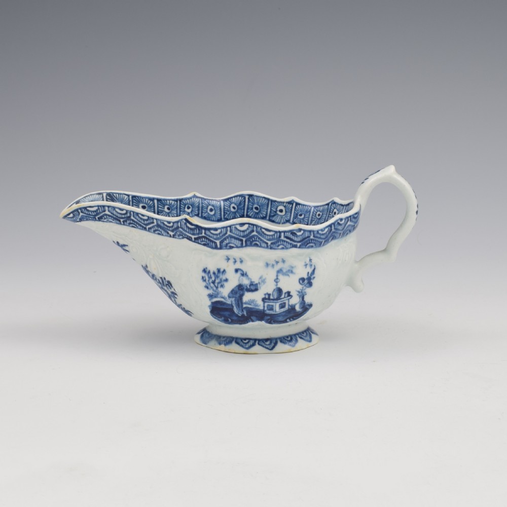 An eighteenth-century English soft-paste porcelain sauce boat decorated with underglaze cobalt blue Chinoiserie figures, a scalloped rim, and a molded handle. View VI