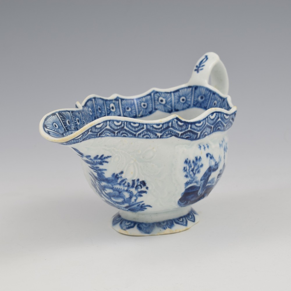 An eighteenth-century English soft-paste porcelain sauce boat decorated with underglaze cobalt blue Chinoiserie figures, a scalloped rim, and a molded handle. View VIII