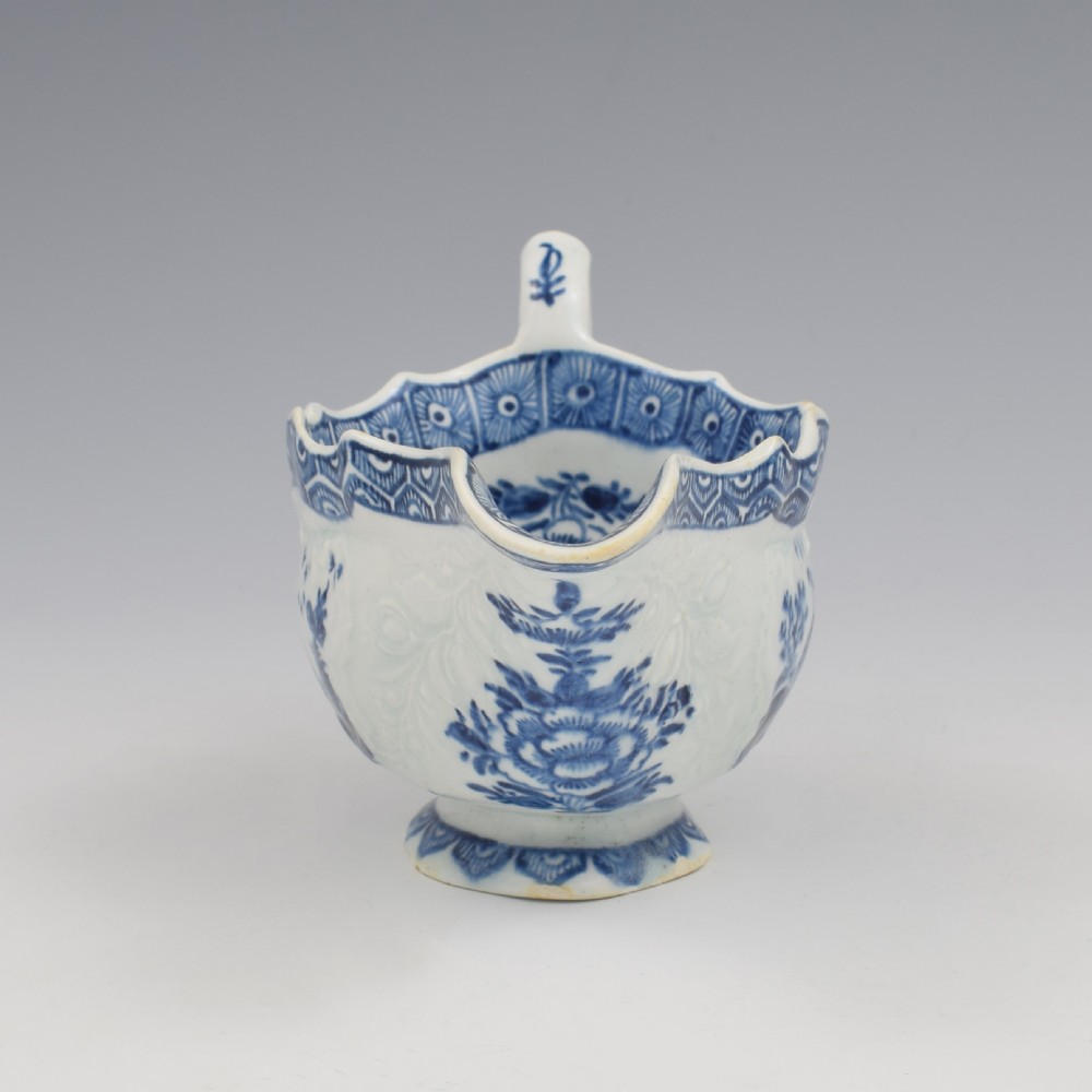 An eighteenth-century English soft-paste porcelain sauce boat decorated with underglaze cobalt blue Chinoiserie figures, a scalloped rim, and a molded handle. View IX