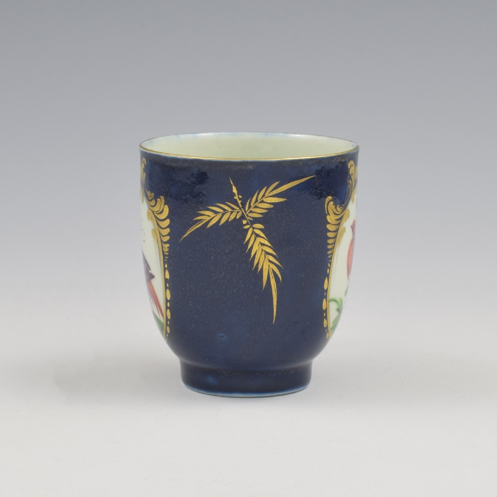 A dark blue soft-paste porcelain coffee cup decorated with a gilded cartouche enclosing a painted exotic bird on a foliage branch. View II