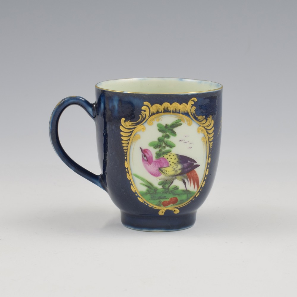 A dark blue soft-paste porcelain coffee cup decorated with a gilded cartouche enclosing a painted exotic bird on a foliage branch. View III