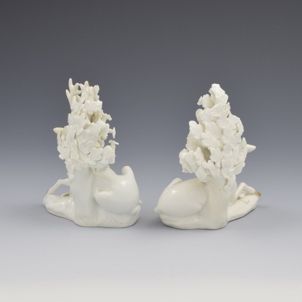 A pair of white glazed porcelain figures representing a recumbent stag and doe with gilded accents set against floral bocage tree backgrounds. View IV