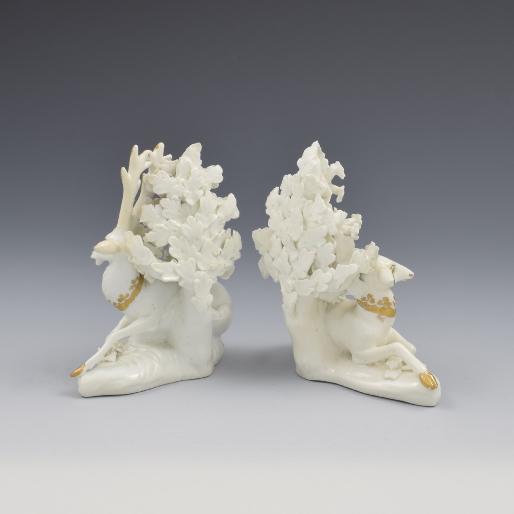 A pair of white glazed porcelain figures representing a recumbent stag and doe with gilded accents set against floral bocage tree backgrounds. View V