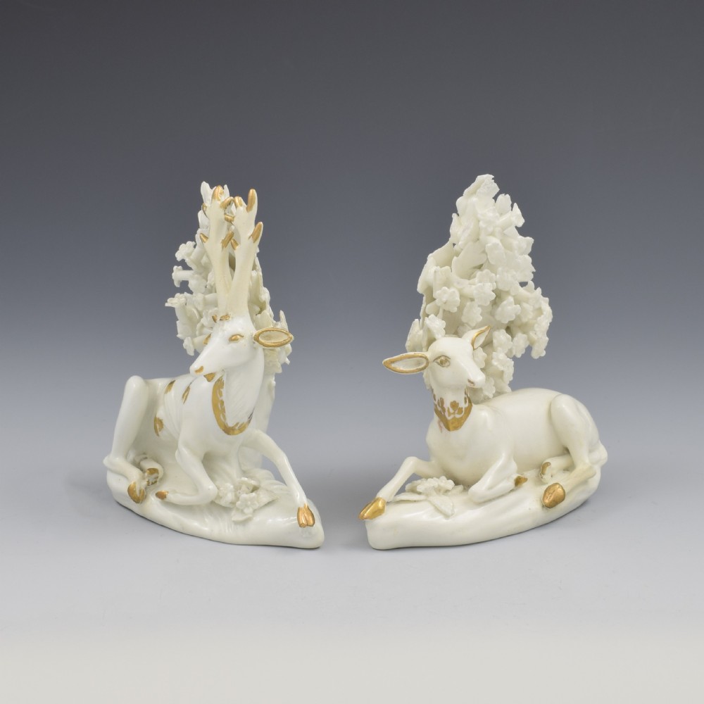 A pair of white glazed porcelain figures representing a recumbent stag and doe with gilded accents set against floral bocage tree backgrounds. View VI
