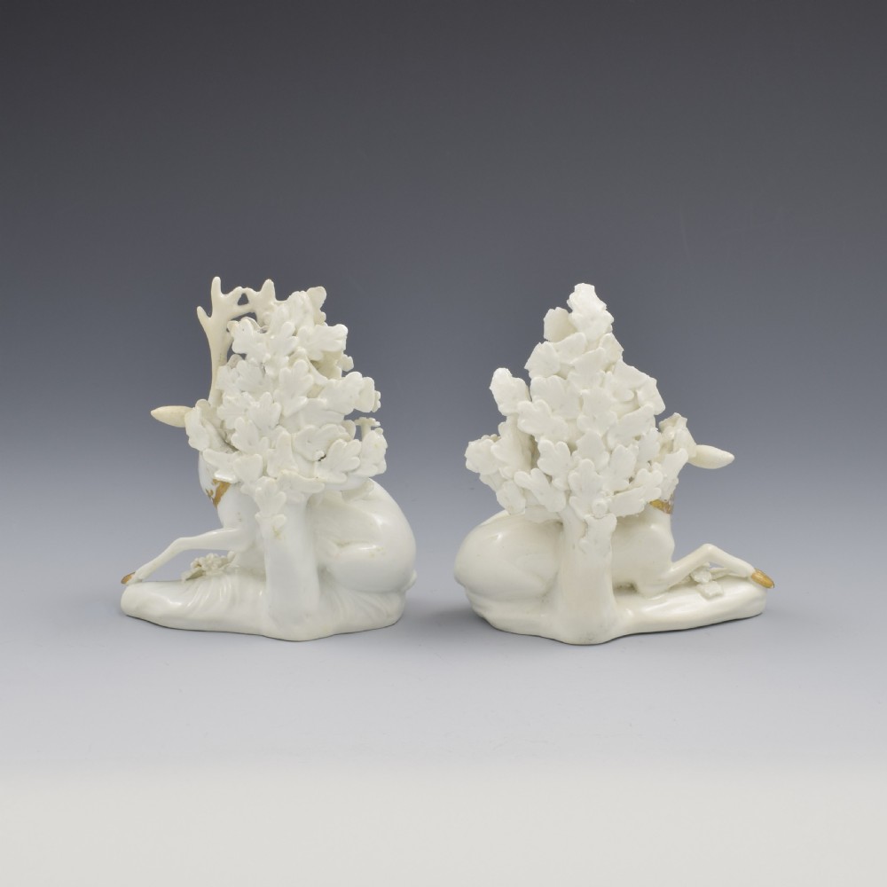 A pair of white glazed porcelain figures representing a recumbent stag and doe with gilded accents set against floral bocage tree backgrounds. View VII
