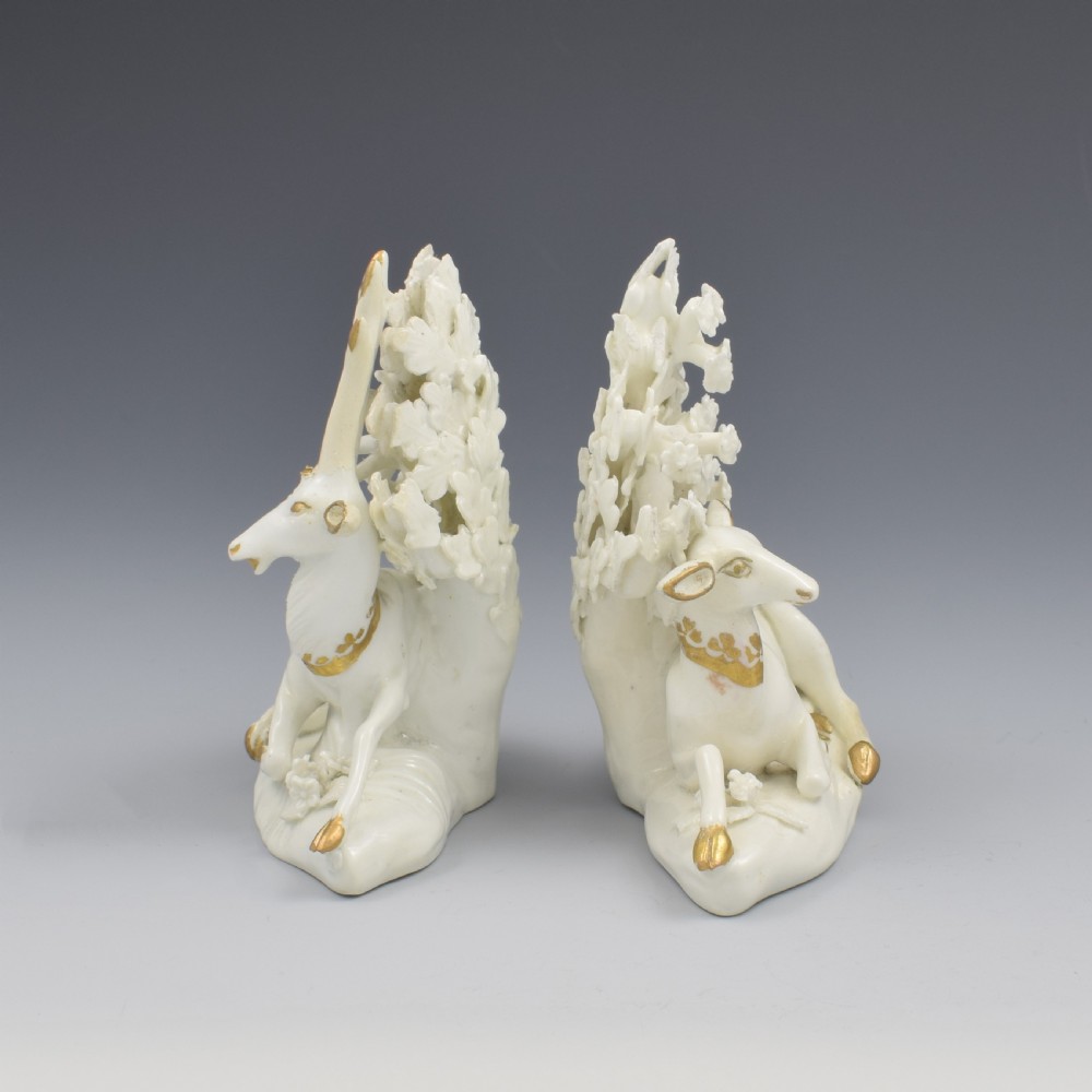 A pair of white glazed porcelain figures representing a recumbent stag and doe with gilded accents set against floral bocage tree backgrounds. View VIII