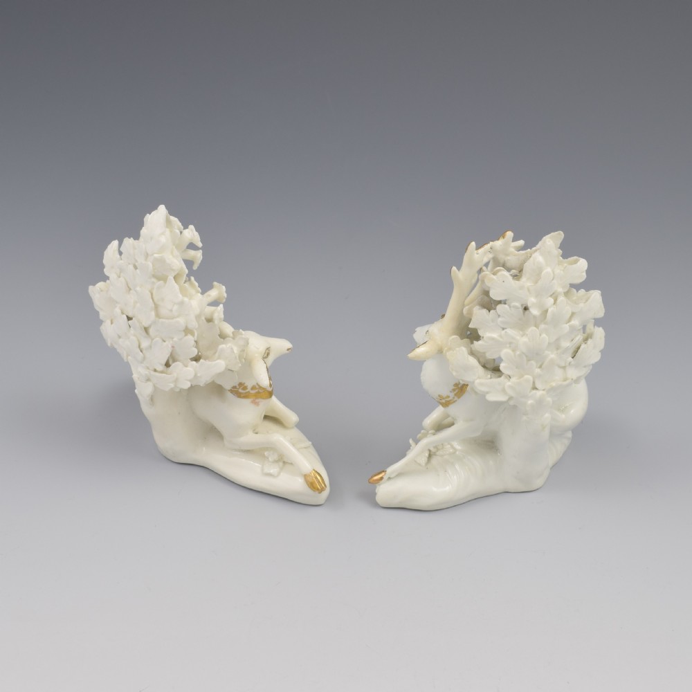 A pair of white glazed porcelain figures representing a recumbent stag and doe with gilded accents set against floral bocage tree backgrounds. View IX