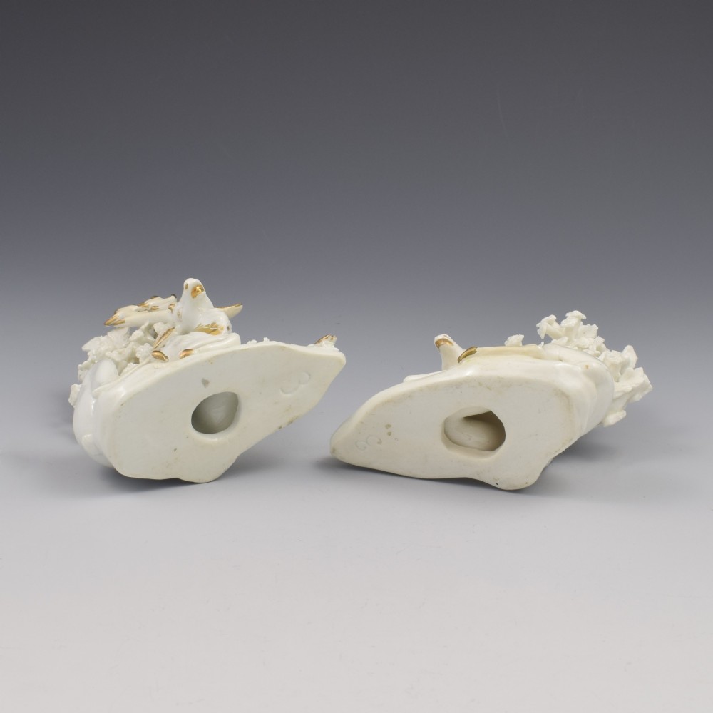 A pair of white glazed porcelain figures representing a recumbent stag and doe with gilded accents set against floral bocage tree backgrounds. View X