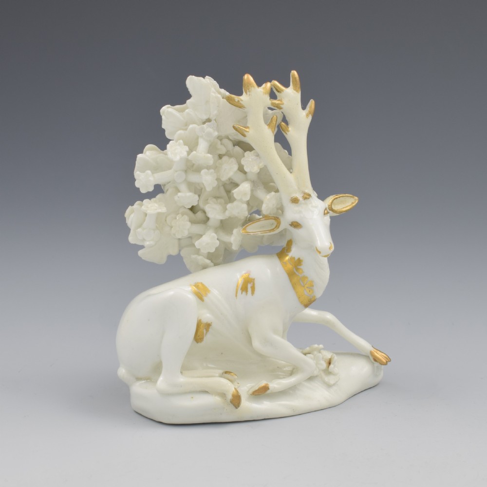 A pair of white glazed porcelain figures representing a recumbent stag and doe with gilded accents set against floral bocage tree backgrounds. View XII