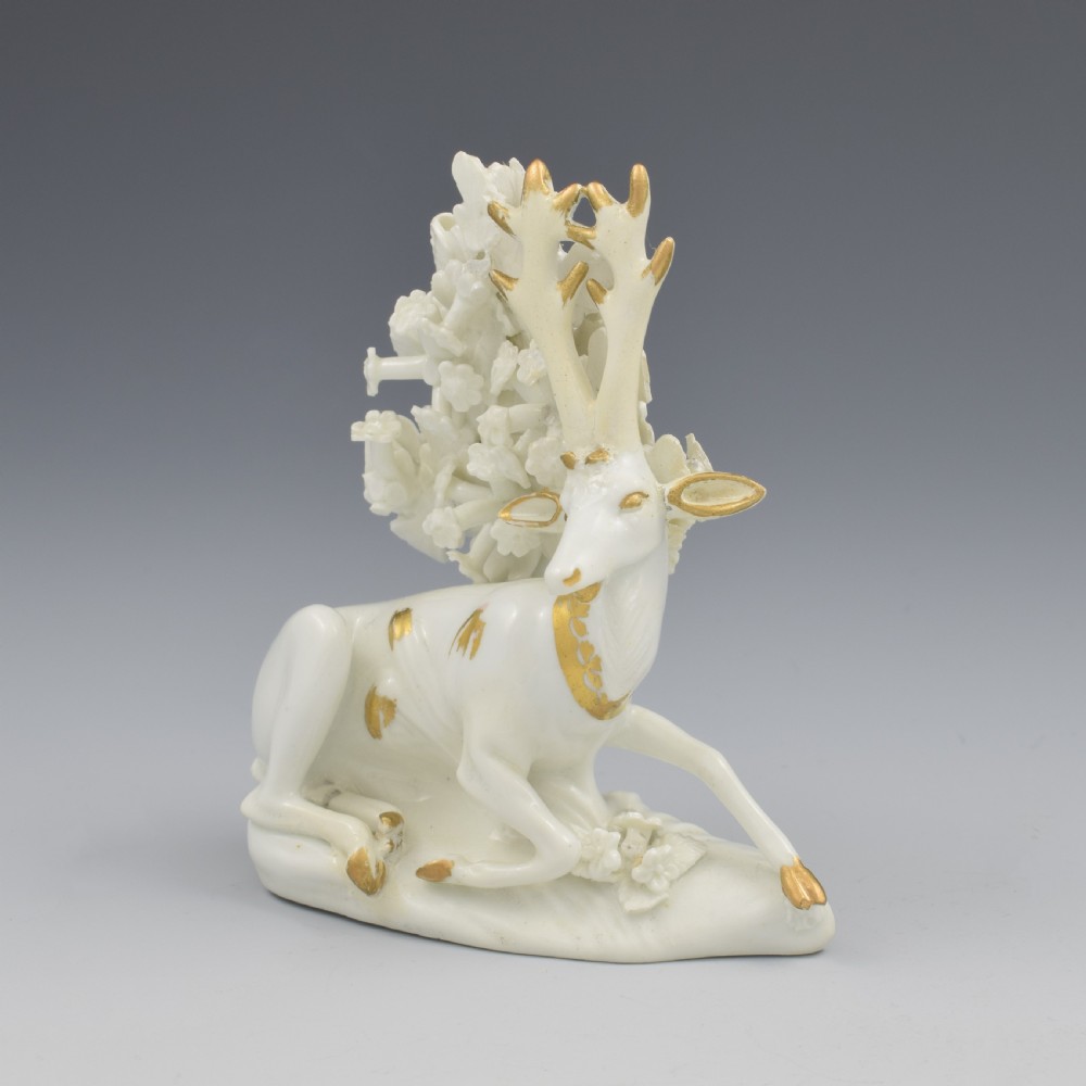 A pair of white glazed porcelain figures representing a recumbent stag and doe with gilded accents set against floral bocage tree backgrounds. View XIII