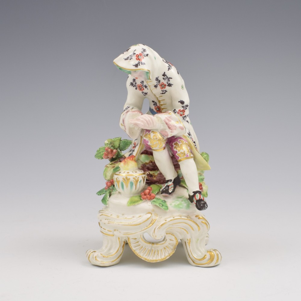 An 18th-century Bow porcelain figure representing Winter, featuring a hooded figure seated on a gilt scrollwork base warming hands over a brazier.