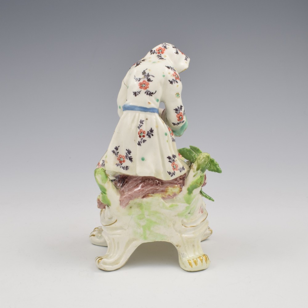 An 18th-century Bow porcelain figure representing Winter, featuring a hooded figure seated on a gilt scrollwork base warming hands over a brazier. View V