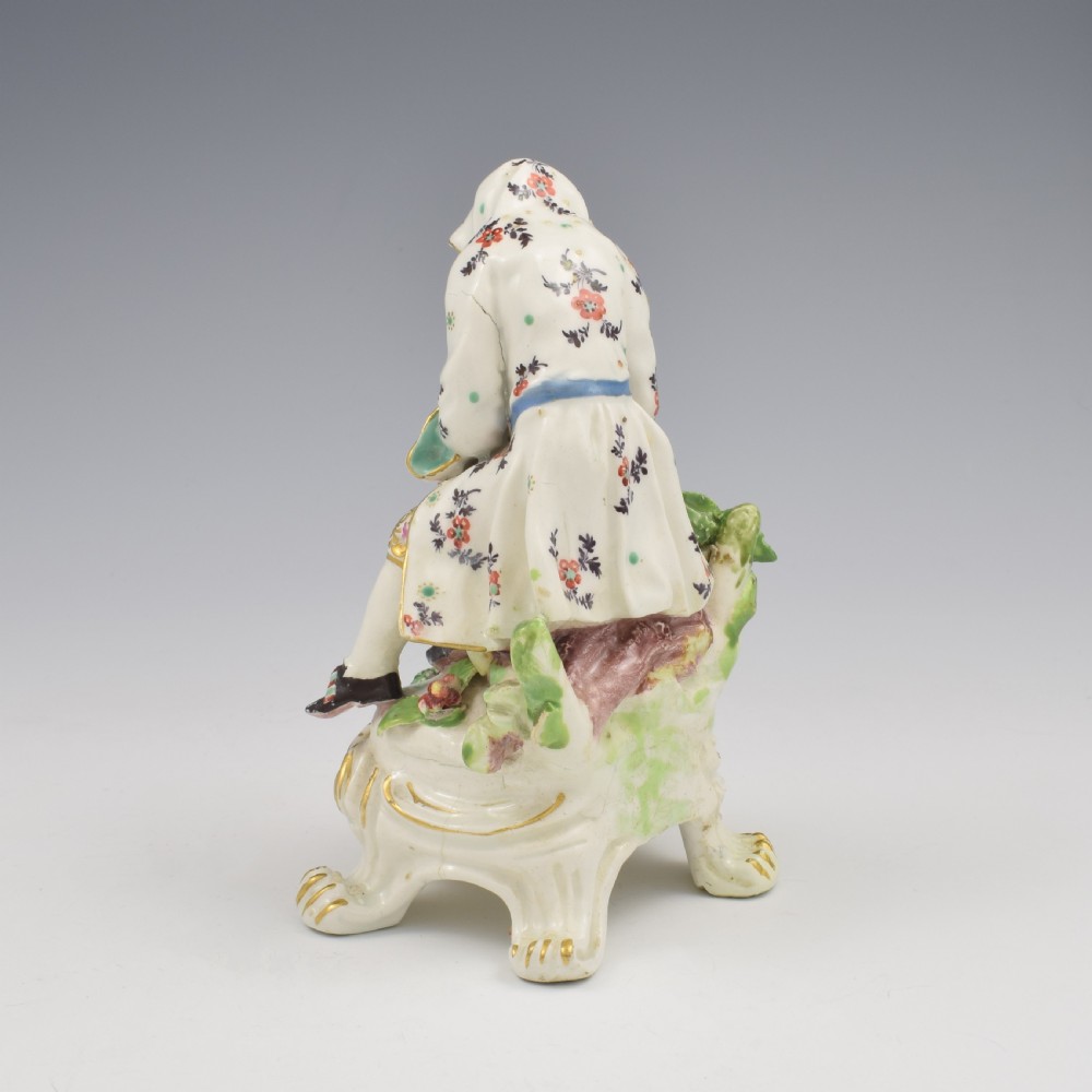 An 18th-century Bow porcelain figure representing Winter, featuring a hooded figure seated on a gilt scrollwork base warming hands over a brazier. View VI