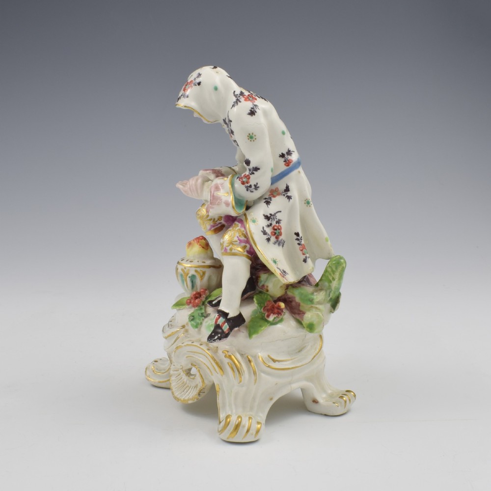 An 18th-century Bow porcelain figure representing Winter, featuring a hooded figure seated on a gilt scrollwork base warming hands over a brazier. View IX