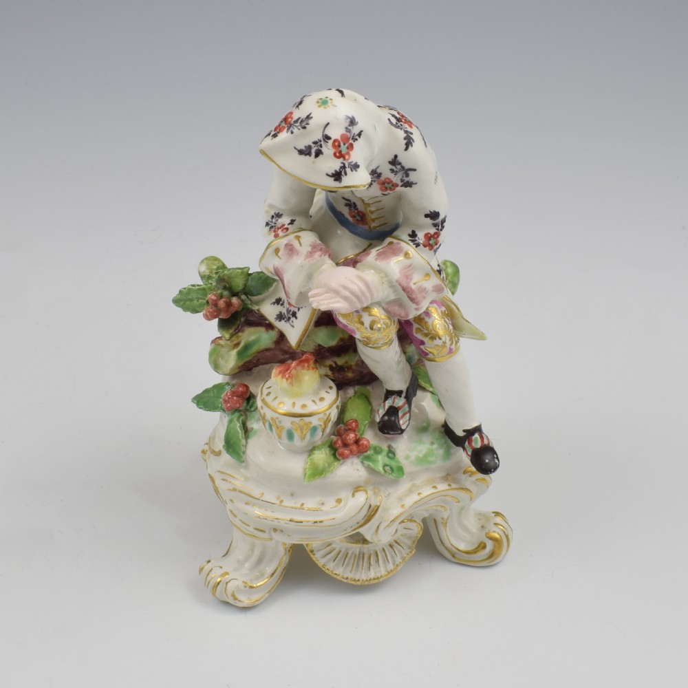 An 18th-century Bow porcelain figure representing Winter, featuring a hooded figure seated on a gilt scrollwork base warming hands over a brazier. View X