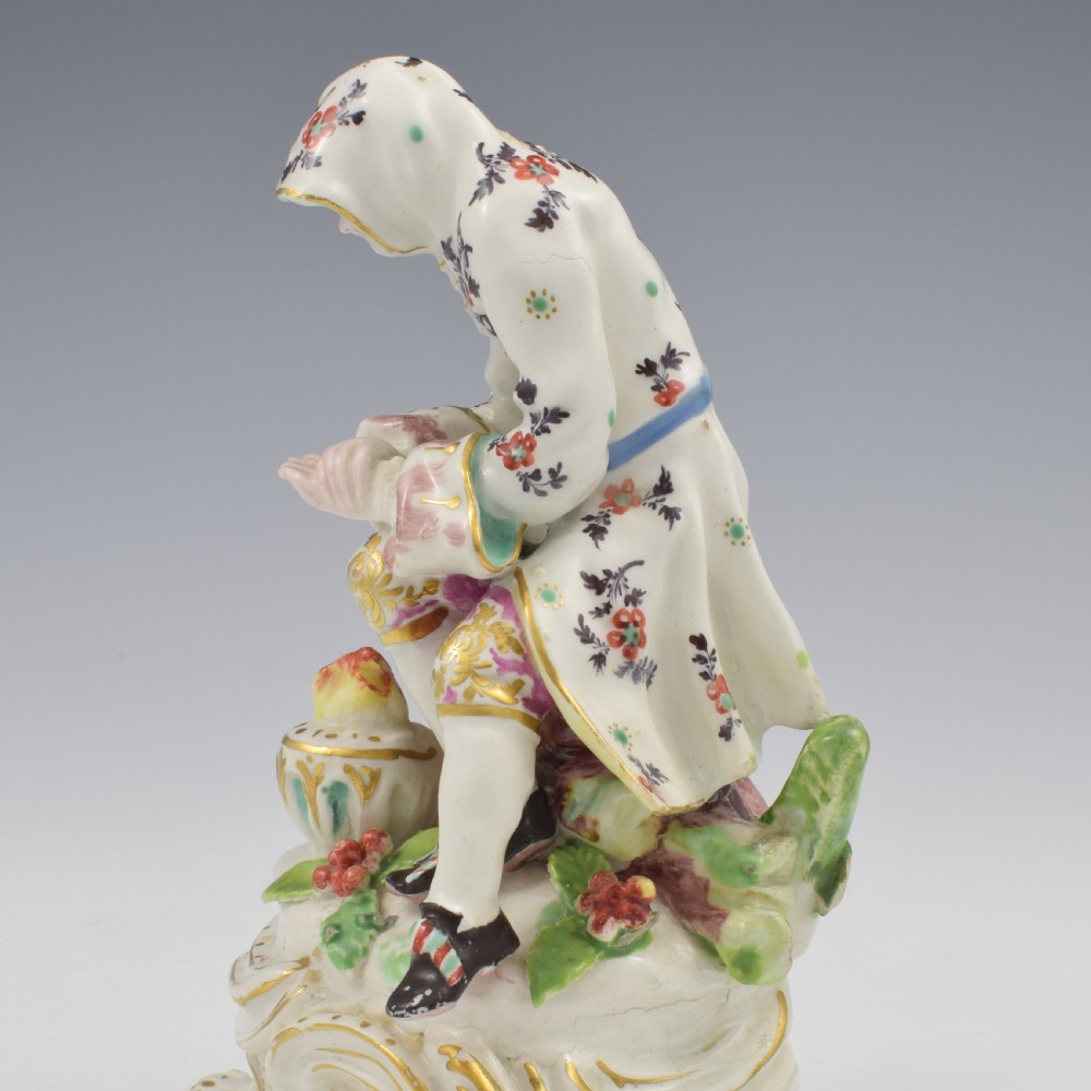An 18th-century Bow porcelain figure representing Winter, featuring a hooded figure seated on a gilt scrollwork base warming hands over a brazier. View XV
