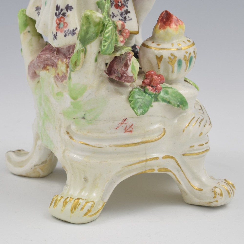 An 18th-century Bow porcelain figure representing Winter, featuring a hooded figure seated on a gilt scrollwork base warming hands over a brazier. View XIX